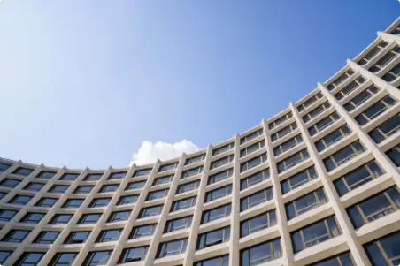Curved modern building with many windows, set against a clear blue sky with a small white cloud.