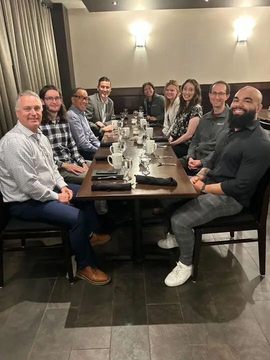 A group of nine people sit around a restaurant table, smiling at the camera.
